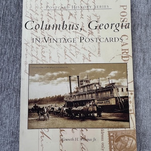 May include: A vintage postcard depicting a steamboat docked at a wharf in Columbus, Georgia. The postcard is titled "Columbus, Georgia in Vintage Postcards" and features the text "Chattahoochee River Wharf, Columbus, Ga." at the bottom. The steamboat is named "Queen City".