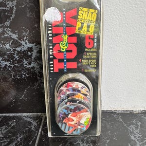 May include: A clear plastic package containing a set of six collectible sports game discs. The package features the text "TONX" and "FOUR SPORT DRAFT." The discs inside display images of basketball players. The package also includes a "SHAO PAO" collectible.