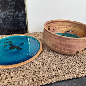 May include: A set of two ceramic bowls with a teal glaze and black accents. The larger bowl has a rounded shape and the smaller bowl is a shallow plate.