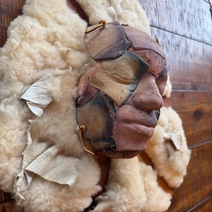 May include: A white ceramic mug with a black handle and the text "But First, Coffee" in a bold, black font. The mug is set against a blurred background, suggesting a cozy setting.