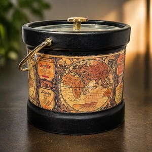 May include: Black and gold ice bucket with a world map design. The bucket has a gold handle and a clear lid with a gold knob. The map is in shades of brown and tan.