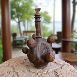 May include: A handcrafted, dark brown wooden bottle with a unique design. The bottle features a long neck and a bulbous body with several spherical, decorative elements. The wood grain is visible, adding to the rustic aesthetic. The bottle is displayed on a textured stone surface.