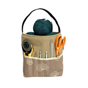 May include: A beige fabric tote bag with a black handle and dandelion print. The bag is filled with yarn, scissors, and crochet hooks.