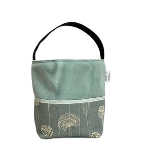 Puede incluir: Una bolsa de tela azul claro con un asa negra y una etiqueta blanca que dice "Stoff & Handwerk". La bolsa tiene un patr&oacute;n geom&eacute;trico blanco y gris en la parte superior y un patr&oacute;n floral azul claro en la parte inferior.