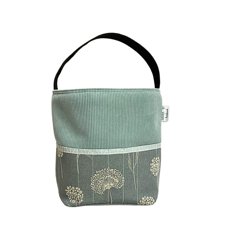 Puede incluir: Una bolsa de tela azul claro con un asa negra y una etiqueta blanca que dice "Stoff & Handwerk". La bolsa tiene un patr&oacute;n geom&eacute;trico blanco y gris en la parte superior y un patr&oacute;n floral azul claro en la parte inferior.