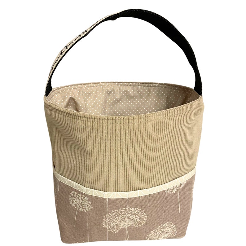 May include: A beige corduroy tote bag with a black handle and a white polka dot lining. The bag has a pocket on the front with a floral pattern.