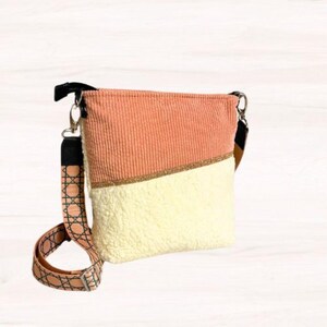 May include: A peach and cream-colored crossbody bag with a patterned strap. The bag is divided diagonally, with peach corduroy on top and cream-colored faux fur on the bottom. A gold glitter strip separates the two sections.