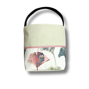May include: A small, green and white fabric tote bag with a black handle. The bag has a floral pattern with pink and green leaves.