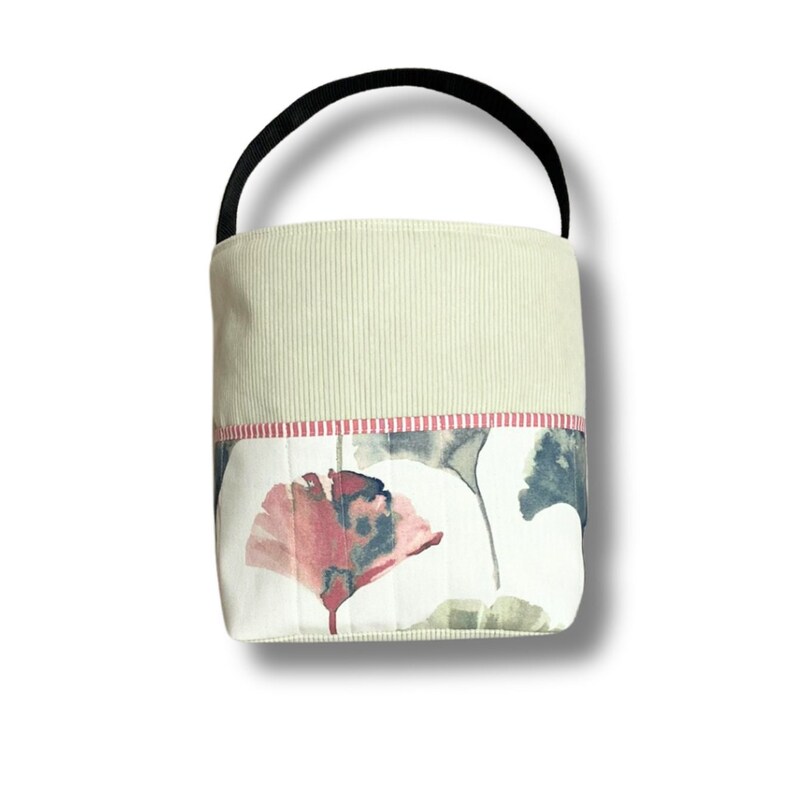 May include: A small, green and white fabric tote bag with a black handle. The bag has a floral pattern with pink and green leaves.