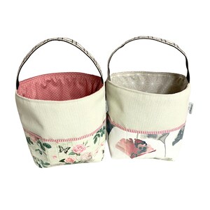 May include: Two fabric storage baskets with handles. One basket has a floral print with butterflies and roses. The other basket has a geometric pattern with ginkgo leaves.