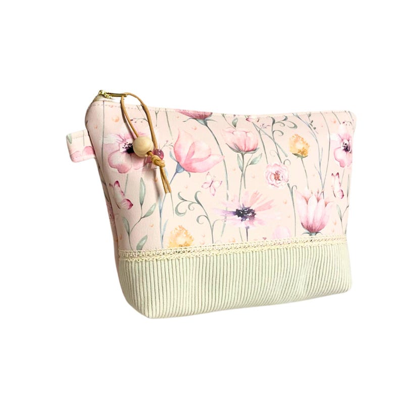 May include: A pink zippered pouch with a floral print and a wooden bead zipper pull. The pouch has a green and white striped bottom with a white lace trim.