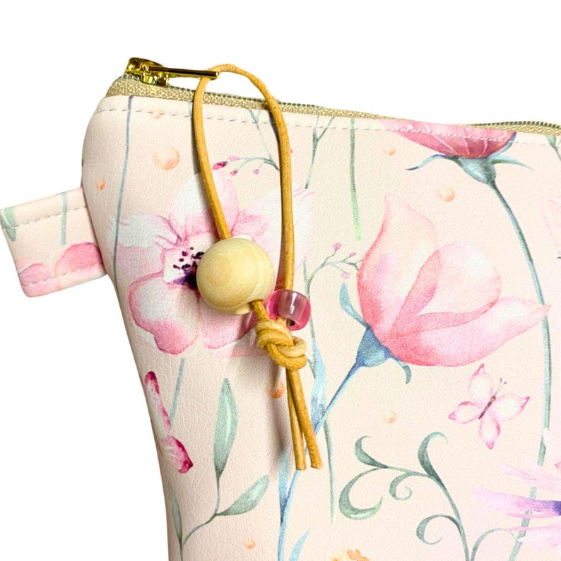 May include: A pink zippered pouch with a floral print and a brown leather tassel with a wooden bead and pink beads.