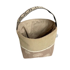 May include: A beige fabric storage basket with a brown and white floral pattern. The basket has a brown fabric lining and a black handle.