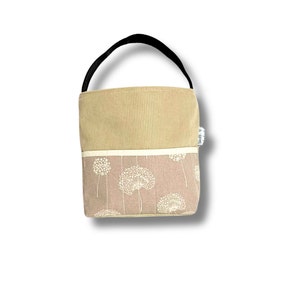 May include: A small beige tote bag with a black handle. The bag has a beige corduroy top and a bottom with a white dandelion pattern on a light pink background. The bag has a white label with the text "Stoff & Stil" on the side.