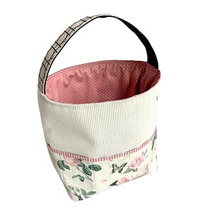 May include: A white and pink fabric storage basket with a black handle and floral print. The basket has a pink polka dot lining and multiple pockets.