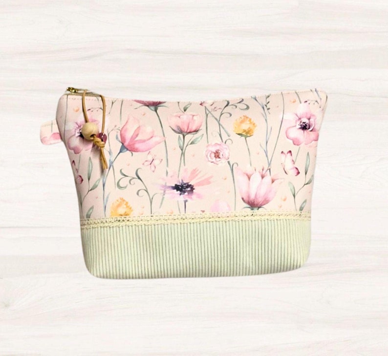May include: A pink floral print zippered pouch with a green and white striped bottom and a brown tassel zipper pull.