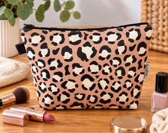 May include: A trapezoidal cosmetic pouch featuring a tan background with a black and cream leopard print pattern. The pouch has a black zipper closure at the top and a small fabric tag on the side with the text Stoff & Stil printed in black.