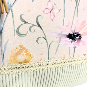May include: A pink fabric with a floral pattern featuring butterflies, flowers, and leaves. The fabric has a white crocheted trim and a white corduroy backing.