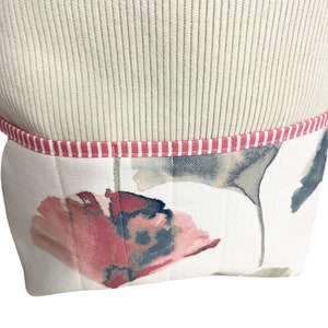 May include: A white fabric storage bin with a pink and white striped trim. The bin has a floral pattern with pink and grey flowers.