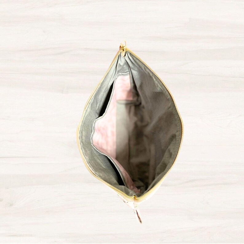 May include: An open zippered pouch with a gray exterior and a pink interior. The pouch is made of a soft, textured fabric.