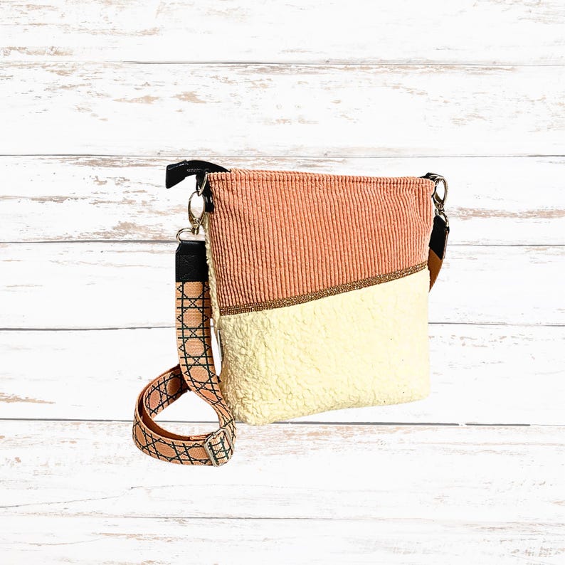 May include: A peach and cream-colored crossbody bag with a patterned strap. The top half is peach corduroy, the bottom half is cream-colored sherpa-like material, and the strap has a geometric design. The bag has a black top and silver hardware.