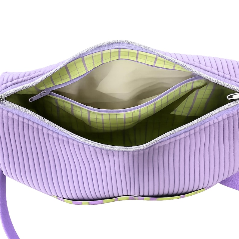 May include: Open view of a lavender corduroy handbag with a silver zipper. The interior features a light beige lining and a green and white plaid pocket. The bag has a matching lavender handle.