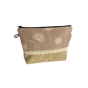 May include: A brown zippered pouch with a floral pattern and a beige lace trim. The pouch is made of a soft, textured fabric.