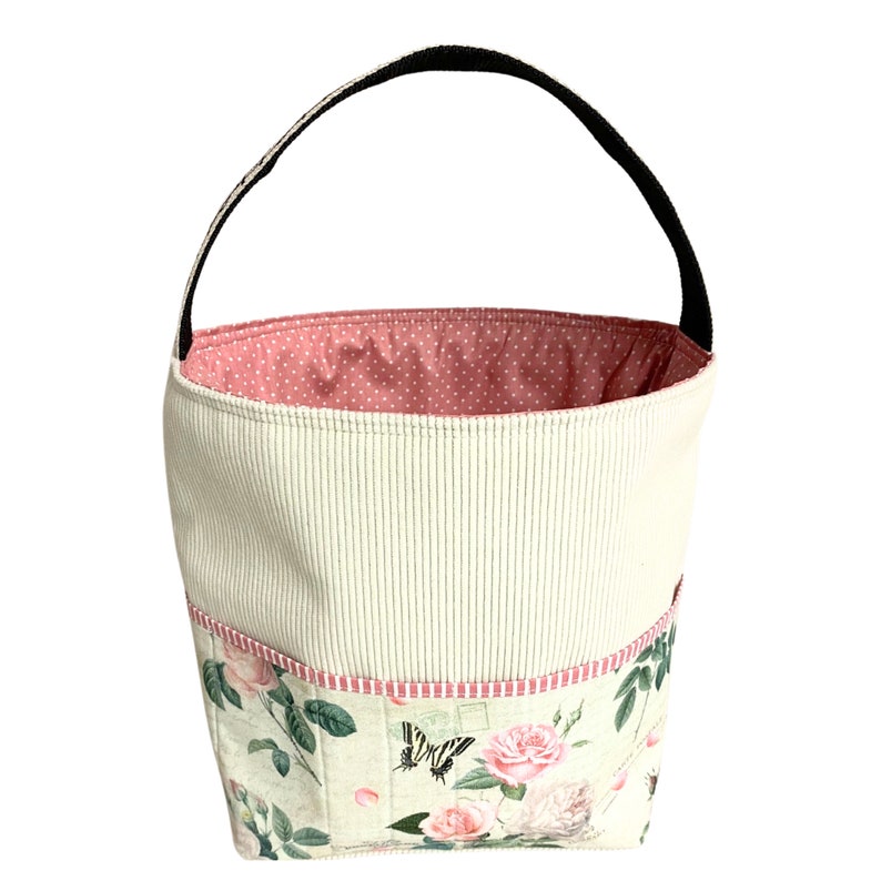 May include: A white fabric tote bag with a pink polka dot lining and a black handle. The bag has a floral print with roses and butterflies.