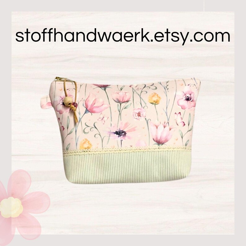 May include: A pink zippered pouch with a floral print featuring pink, yellow, and green flowers. The pouch has a green and white striped bottom and a gold zipper pull with a brown tassel.