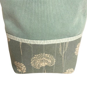 Puede incluir: Una bolsa de tela azul verdosa con un estampado floral blanco. La bolsa tiene una solapa superior con un ribete blanco.