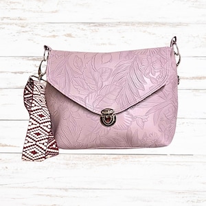 May include: A lilac crossbody bag with a floral embossed pattern. It has a flap closure with a silver clasp and chain strap. A patterned strap in burgundy and white is attached to the side.
