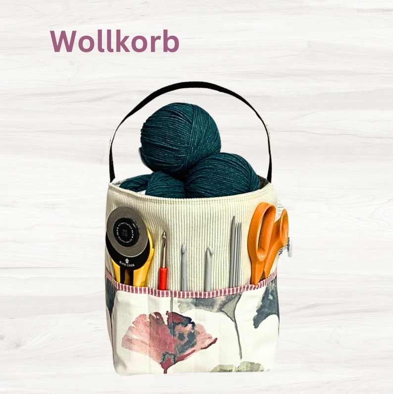 May include: A white fabric storage basket with a black handle, filled with green yarn balls and various knitting needles. The basket has a floral pattern and the text "Wollkorb" is printed on the top.
