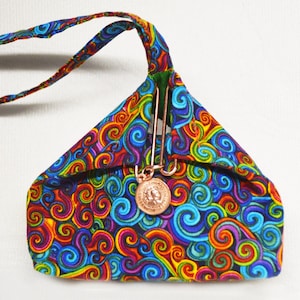 Peut inclure: Un petit sac en tissu coloré avec un motif en spirale. Le sac a un fermoir de couleur cuivre et une longue sangle.