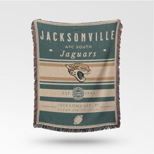 May include: A woven throw blanket featuring the Jacksonville Jaguars logo and team name. The blanket is primarily teal and tan with the team's logo, the words "Jacksonville Jaguars", and the text "EST. 1995". The blanket has a fringed edge.