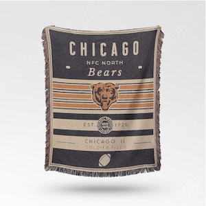 May include: A woven throw blanket featuring the text "CHICAGO" and "BEARS" in a vintage style. The blanket has a bear logo, horizontal stripes, and the text "EST. 1920". The bottom of the blanket reads "CHICAGO, IL SOLDIER FIELD" with a football graphic.
