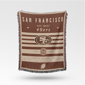 May include: Brown and tan woven throw blanket with the words "SAN FRANCISCO" and "49ers". The blanket features the team logo, stripes, and the text "EST. 1946". The bottom reads "SANTA CLARA, CA LEVI'S STADIUM".