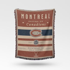 Puede incluir: Una manta rectangular con un fondo marrón rojizo y rayas color crema. La manta presenta el texto "MONTREAL" y "Canadiens" en letras color crema, junto con el logotipo del equipo y el texto "EST. 1917".
