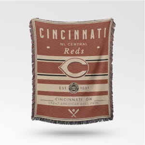 Op de afbeelding: Een rechthoekige deken in rood- en beigetinten, met de tekst "CINCINNATI" en "Reds". De deken heeft het logo van het team, strepen en de tekst "EST. 1881". Het heeft franjes. Ideaal voor honkbalfans.