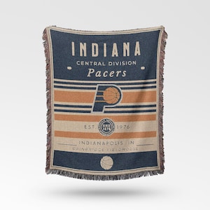 Könnte beinhalten: Eine gewebte Decke in Marineblau und Beige mit dem Logo und dem Namen der Indiana Pacers. Die Decke hat einen Fransenrand und enthält den Text "INDIANA", "Pacers" und "EST. 1976". Das Design enthält orangefarbene und beige Streifen.