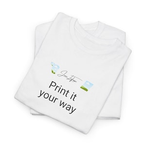Könnte beinhalten: Zwei weiße T-Shirts übereinander gestapelt. Das obere Shirt trägt den schwarzen Text "Print it your way", eine Signatur und kleine Landschaftsgrafiken. Die Shirts sind sauber gefaltet.