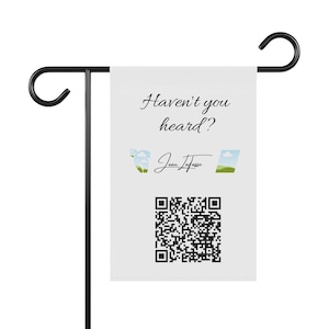 May include: A white garden flag with the text "Haven't you heard?" and the name "Jean Jafasse" in script. The flag also features a QR code and small landscape illustrations. The flag is mounted on a black metal stand.