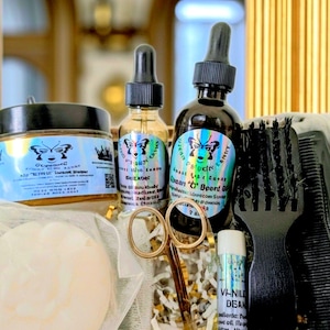 May include: A gift basket with hair and beard care products. Includes two bottles of oil, a jar of cream, a lip balm, scissors, and combs. The labels feature a butterfly design and text. The products are arranged on a bed of shredded paper.