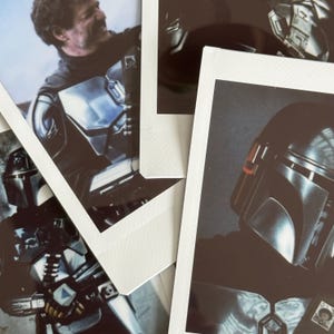 May include: A collection of polaroid-style photographs featuring images of a character in metallic armor. The images show the character's helmet and parts of the armor. The photos are arranged on a light-colored surface.