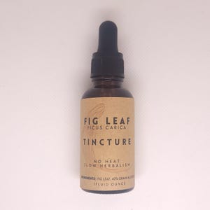 Puede incluir: Una botella de vidrio marrón con un gotero y una etiqueta de papel marrón. La etiqueta dice "Fig Leaf Ficus Carica Tincture No Heat Slow Herbalism Ingredients: Fig Leaf, 40% Grain Alcohol 1 Fluid Ounce".