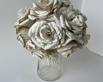 May include: A bouquet of white paper roses made from the pages of a book. The roses are arranged in a clear glass vase.
