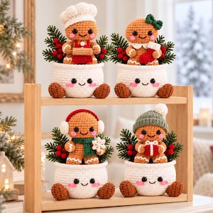 May include: Four crocheted gingerbread figures sit inside white crocheted bowls with smiling faces. Each figure features unique accessories including a chef hat, green bow, red earmuffs, or green beanie, along with festive greenery and red berries.