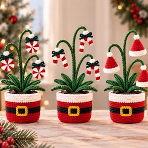 May include: Three crocheted potted plants with green leaves and red and white Christmas-themed ornaments. Each pot is red with a black belt and yellow buckle design. The plants feature peppermint candies, candy canes, and Santa hats as blooms.