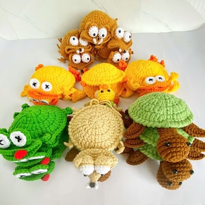 May include: A collection of handmade crochet plush toys featuring various animal shapes including turtles and frogs. The toys are crafted in vibrant colors such as green, yellow, tan, and brown, with prominent white and black stitched eyes.
