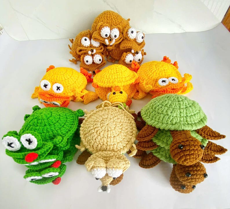 May include: A collection of handmade crochet plush toys featuring various animal shapes including turtles and frogs. The toys are crafted in vibrant colors such as green, yellow, tan, and brown, with prominent white and black stitched eyes.