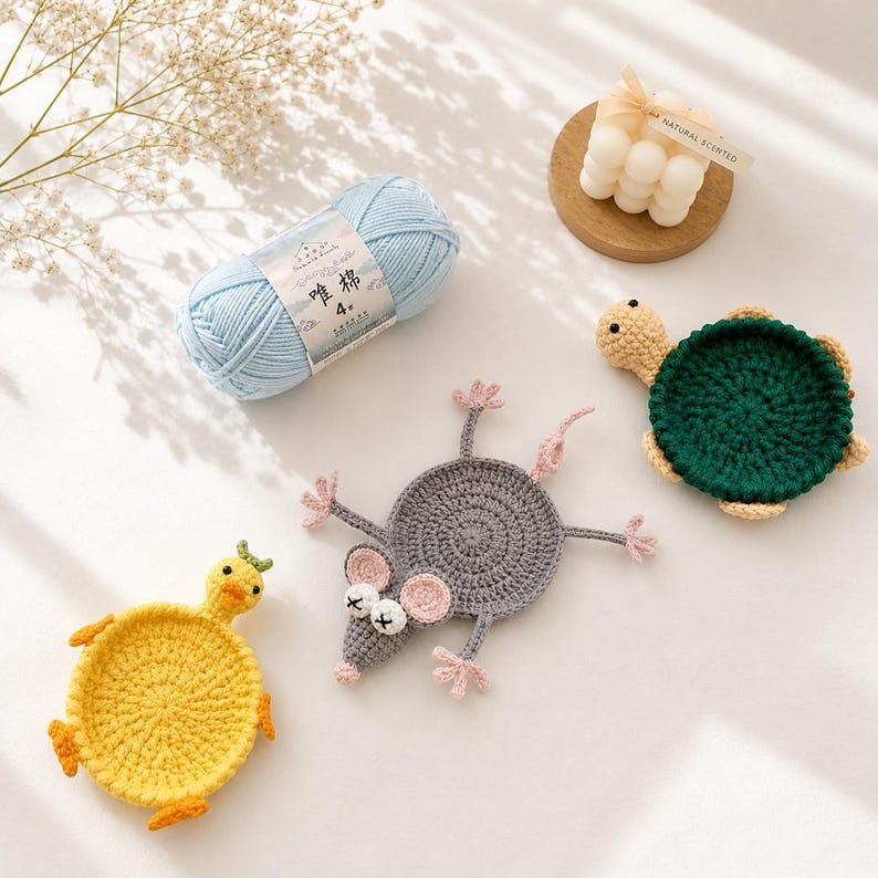 May include: A light blue yarn skein with a label reading 唯棉 4, a white bubble candle on a wooden base, and three crocheted coasters shaped like a yellow duck, a gray mouse with pink ears, and a dark green turtle with a light tan head and feet.